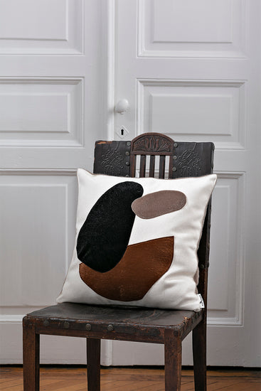 Minimalistic throw pillow cover with simple brown and black embroidered design placed on a old wodden chair