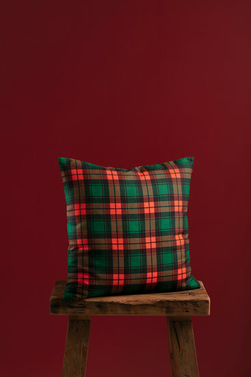 Handmade tartan plaid pillow cover with green and red checkered design, styled on a rustic wooden bench with a festive red backdrop.